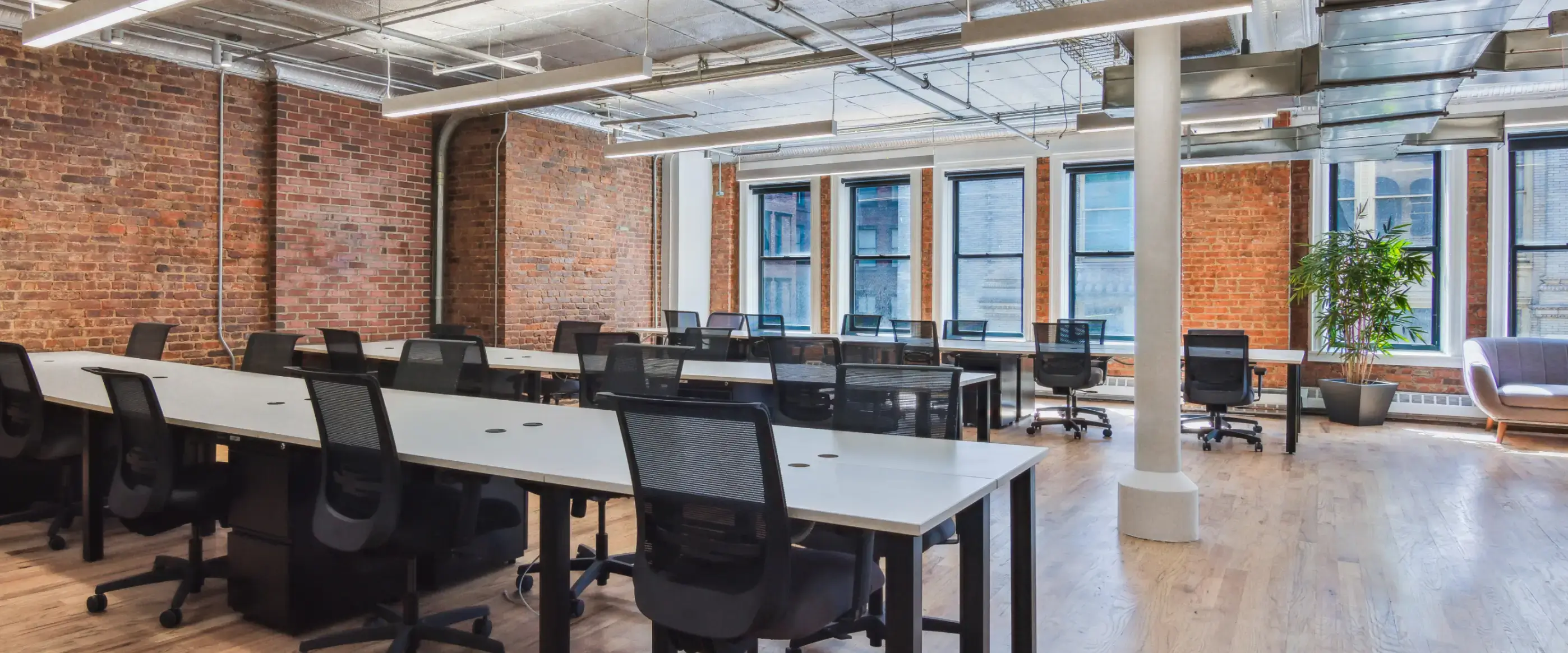 Large, open coworking space with rows of desks and chairs. Beautiful brick walls and large windows surround.