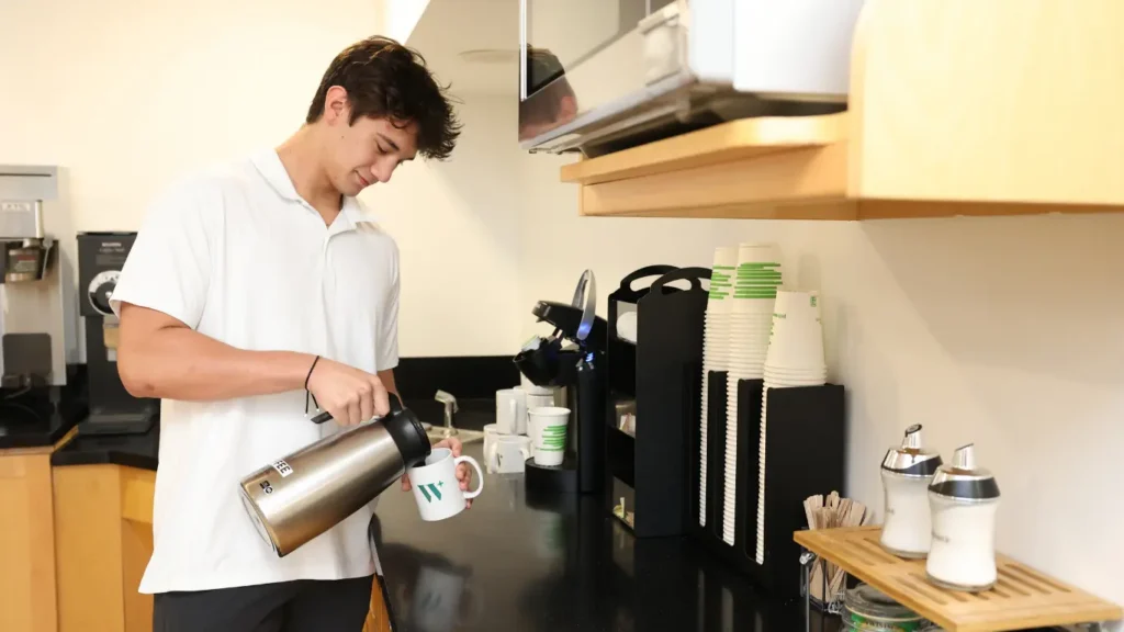 Man pouring coffee into a mug in an office kitchen area.