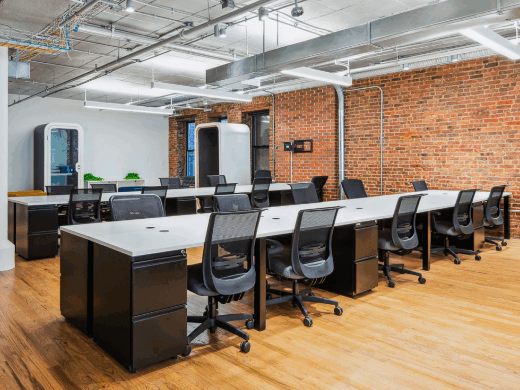 A modern coworking space in Chelsea with long desks, chairs, and brick walls.