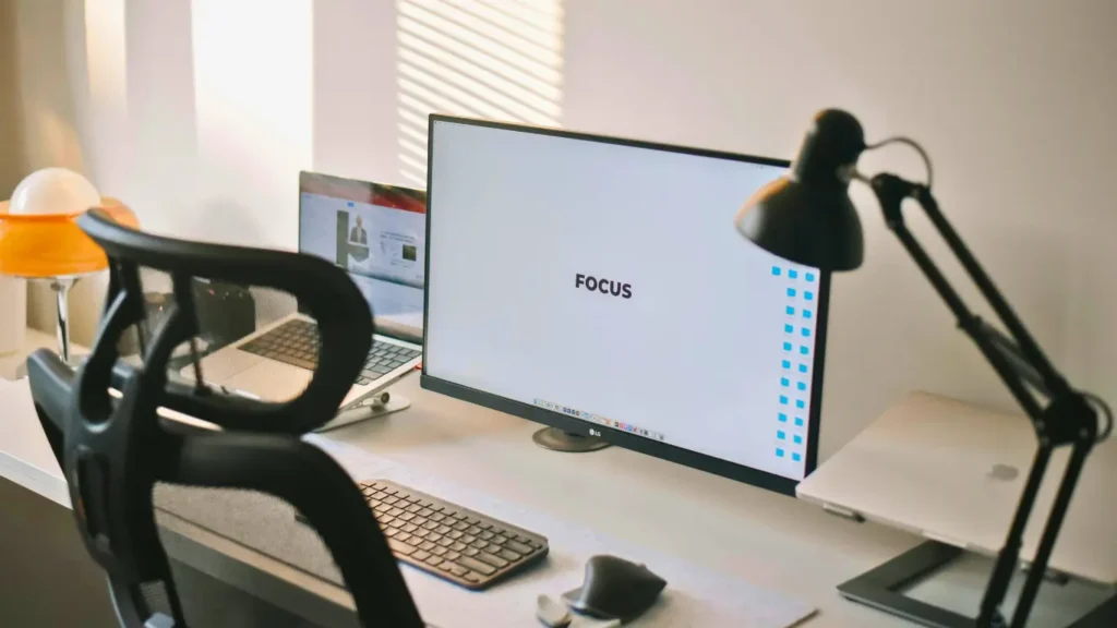Ergonomic mesh office chair at a clean workstation with dual monitors and task lighting.