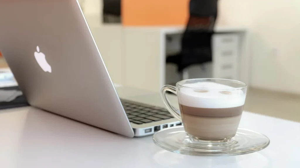 Laptop and coffee at a bright coworking desk.
