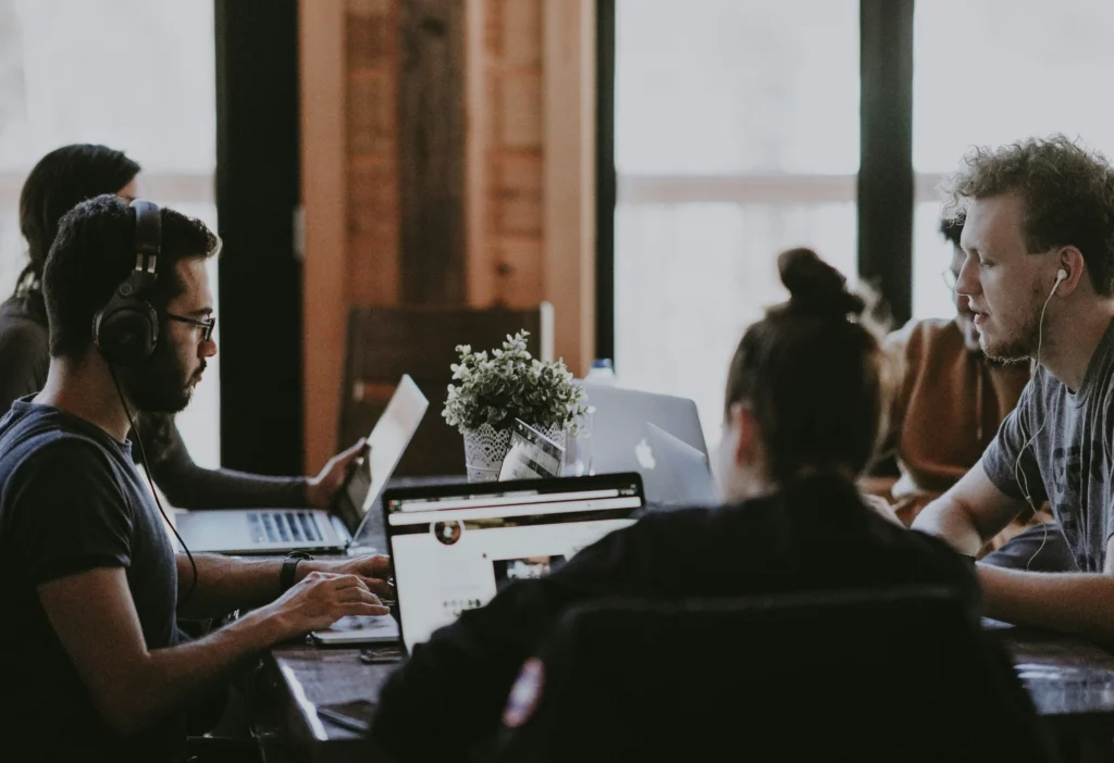 Small team, a part of hybrid work model NYC, collaborating at a shared table with laptops in a cozy workspace.