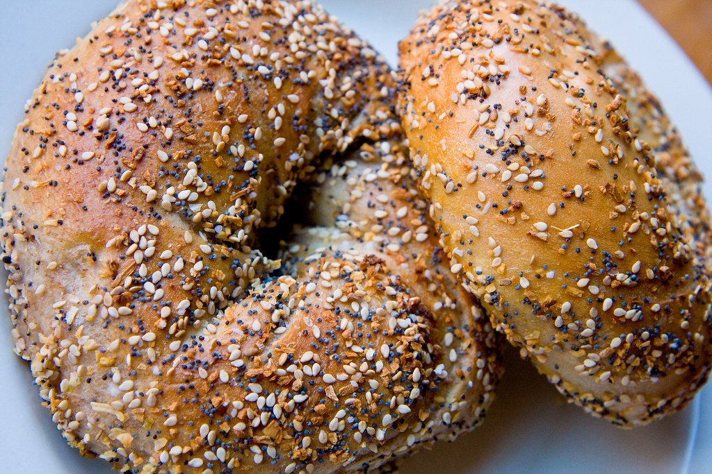 Two everything bagels on a white surface.