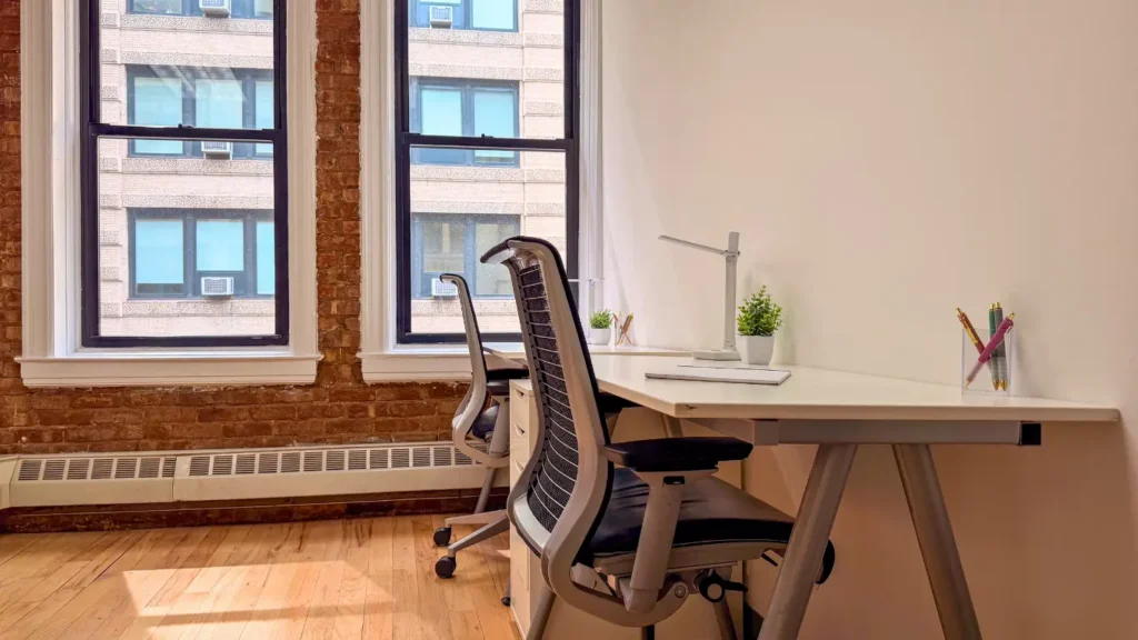 Example of a productive workspace: Bright private office with large windows, exposed brick walls, and two workstations arranged to maximize natural light.