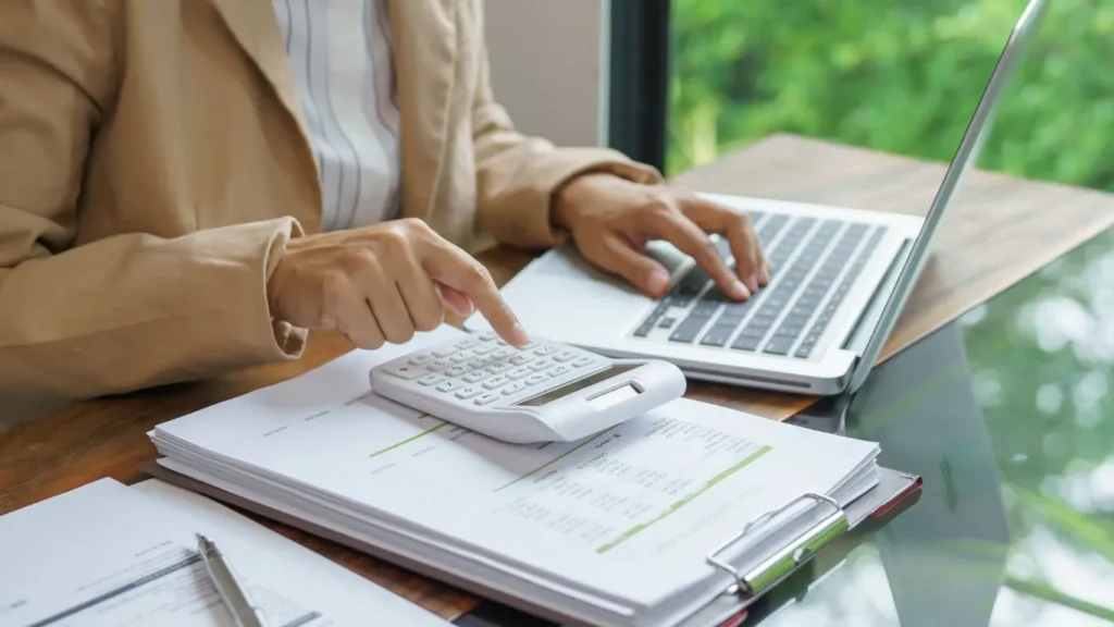 Person using calculator and laptop to review business expenses