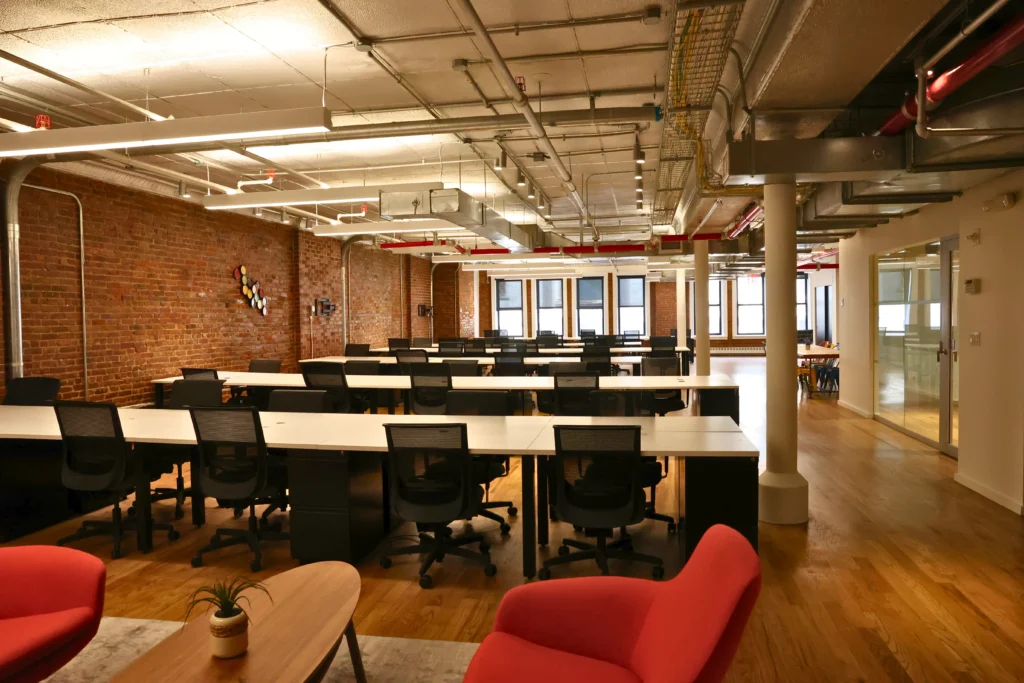 Large open coworking space with rows of desks and exposed brick walls.